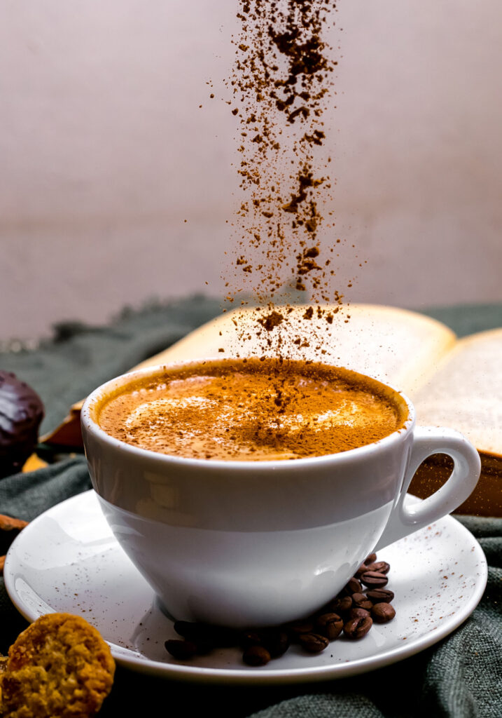 A cup of cappuccino with frothy milk, placed on a table alongside cookies and an open book.