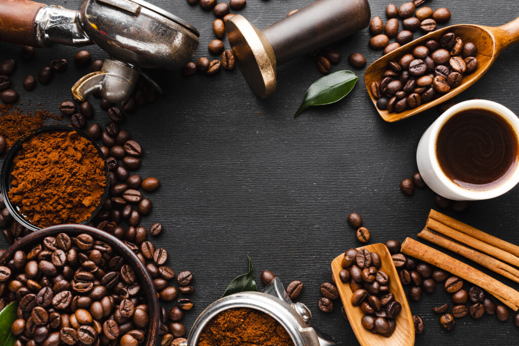 Top view of various coffee accessories including a portafilter, coffee grinder, coffee beans, and a cup of hot coffee arranged on a wooden table.